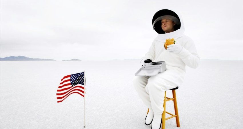 Fotografi ilustruese e një astronauti në hapësirë duke konsumuar hamburger.