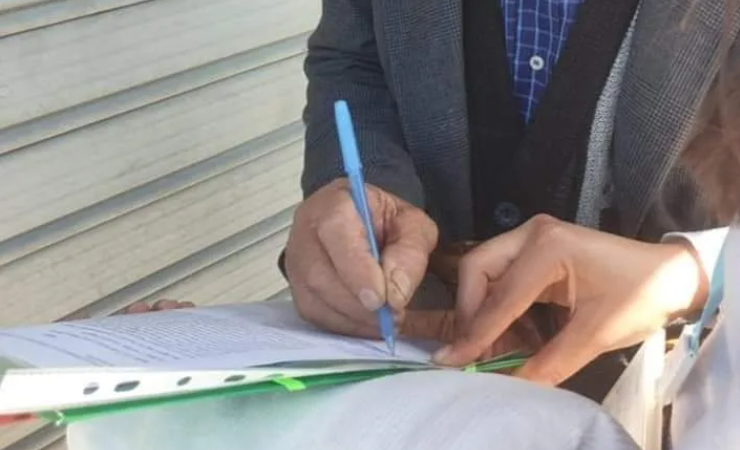 Fotografi ilustruese e një të moshuari që po firmos një peticion.